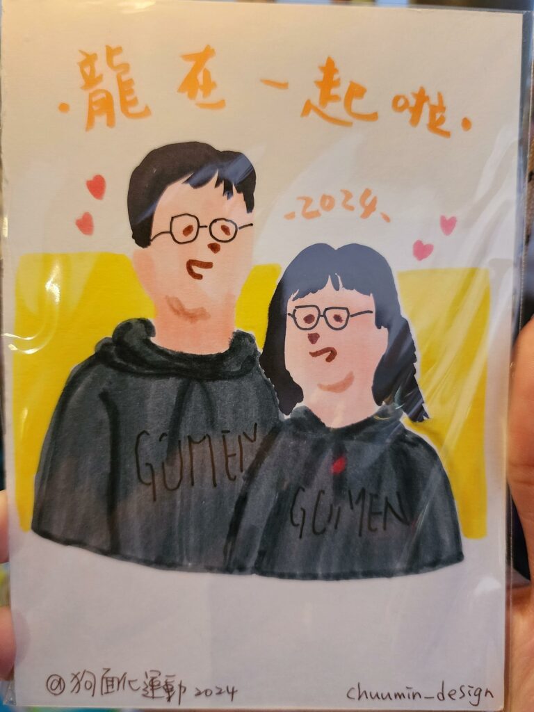 This image is another hand-drawn piece, depicting two people side by side, with a simple and colorful background. The two figures appear to be wearing matching black hoodies with the word "GOMEN" written across. This word is often used in Japanese to mean "sorry" or "excuse me". Both individuals have glasses, and there's a semblance of a smile on their faces. The person on the left has short hair, while the one on the right has longer hair. The Chinese characters at the top of the image again say "新年快乐", which translates to "Happy New Year", accompanied by a couple of small heart shapes. The year "2024" is noted below the greeting, suggesting this drawing is possibly another New Year’s card for the year 2024. The signature at the bottom, "chuanmin_design 2024", suggests the creator's name or brand and the year it was made. This style of artwork has a casual and friendly vibe, indicating it might be intended for a personal greeting card or a casual gift among friends or family. The illustration is simple, focusing on the warmth and cheerful expressions of the characters to convey a message of happiness and good wishes for the New Year.