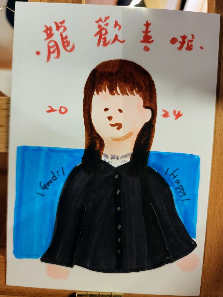 This image shows another hand-drawn character with a cheerful expression. The character has straight, shoulder-length hair and is wearing a dark blouse with a Peter Pan collar and buttons down the front. Behind the character, there is a background split into two sections with white on the top and a blue rectangle on the bottom left, which has the word "Good!" written on it, suggesting a positive theme. The same Chinese characters appear as in the previous images, "笑顔満点" at the top, meaning "Full of Smiles" or a similar positive sentiment, and "の次の代たる者" at the bottom, which can be translated as "The Next Generation" or "Person of the Next Era." The number "2024" is written in red, likely indicating the year of creation. On the right side of the blue rectangle, "Happy" is written, reinforcing the positive tone. The style and theme suggest that it's part of a series made by the same artist, indicated by the "chuum!n- design" signature seen in the previous images.